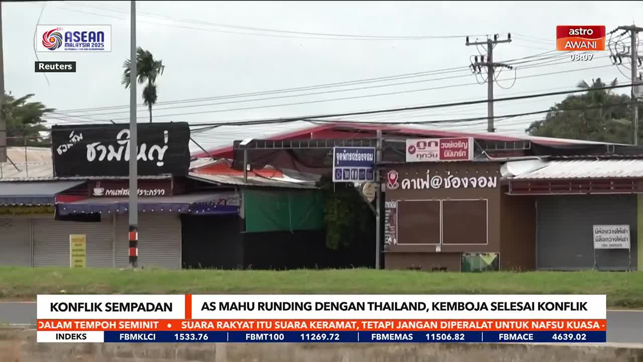 Across the road, a row of closed-up shops sits beneath a cloudy sky, the signs above them in Thai.  Astro Awani's news ticker at the bottom of the screen reports on border conflict.

