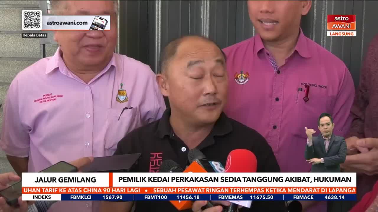 A man in a black shirt speaks into several microphones, while two others in pink shirts stand beside him. The Astro Awani logo is visible in the corner, and a sign language interpreter gestures on a small screen.
