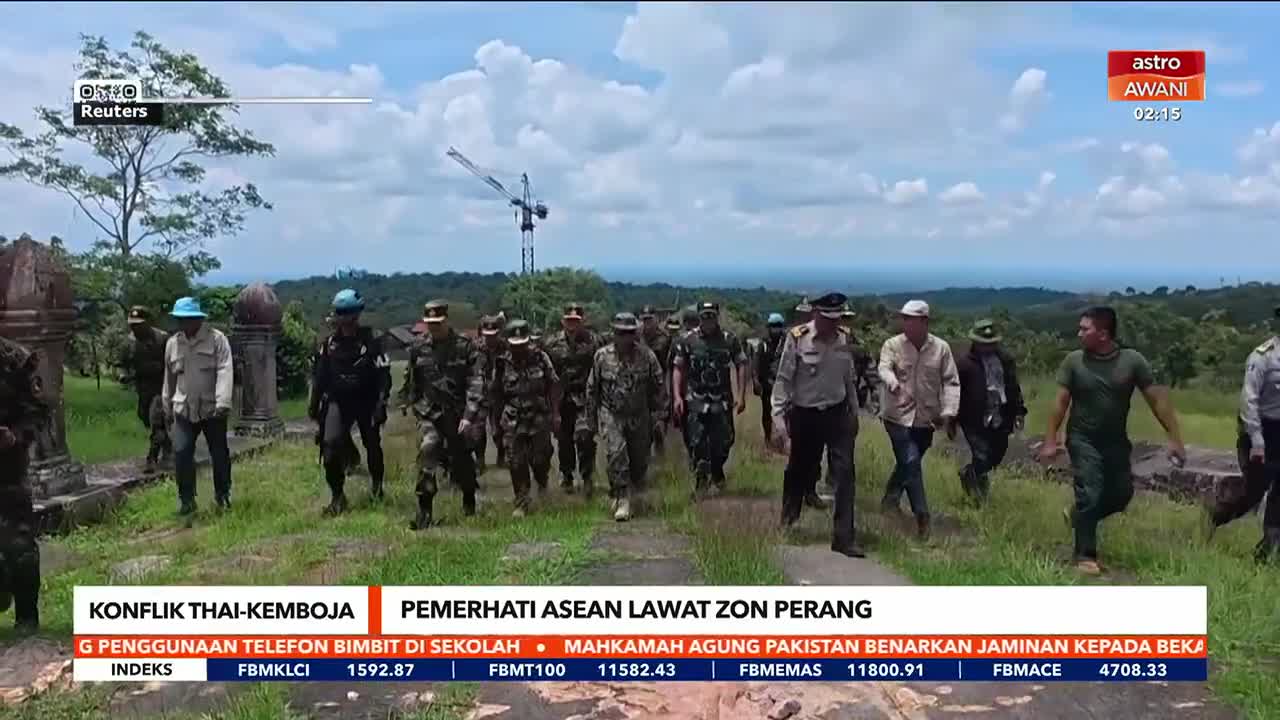 A group of men in various uniforms and civilian clothes walk across a grassy area. The scene is being covered by Astro Awani, with a Reuters logo visible in the corner.
