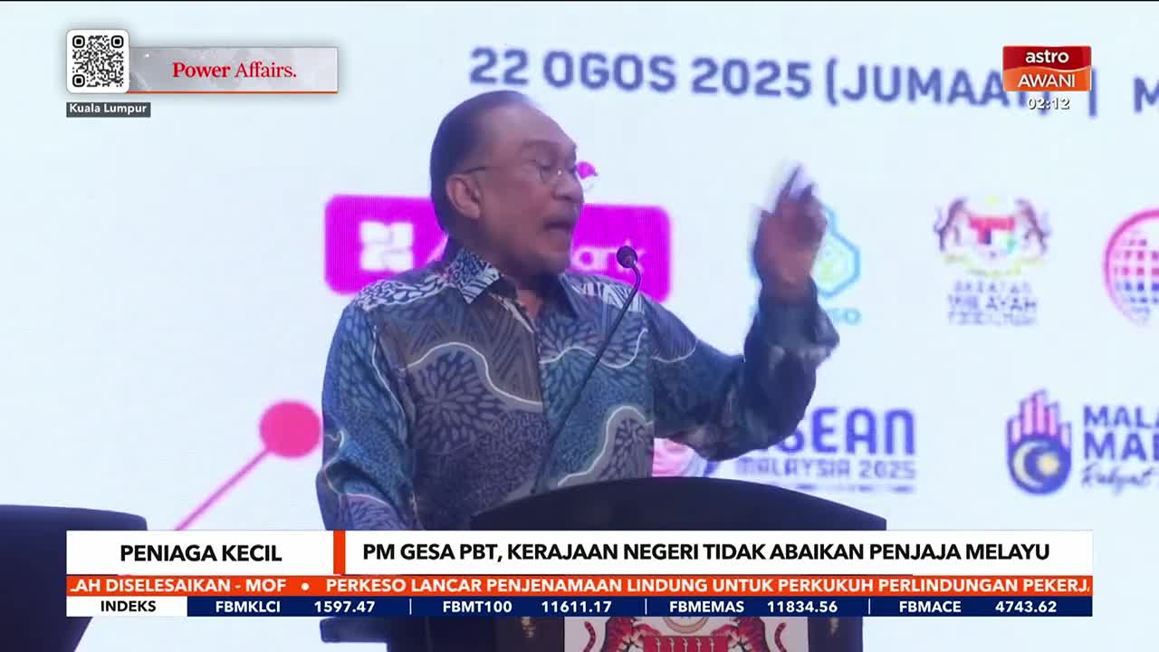 A man in a patterned shirt gestures emphatically, speaking into a microphone on a stage. The Astro Awani logo is visible in the corner, and a screen behind him displays text and graphics related to Malaysia.
