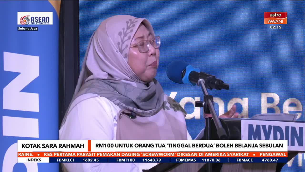 A woman in a headscarf speaks into a microphone, her hands gesturing slightly as she addresses the camera. The Astro Awani logo is visible in the corner, and a news ticker scrolls across the bottom of the screen.
