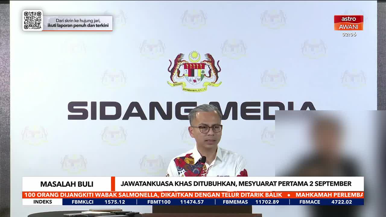 A man in glasses and a patterned shirt speaks at a press conference, the words "SIDANG MEDIA" large behind him. The Astro Awani logo is visible in the top right corner, and financial data scrolls at the bottom of the screen.
