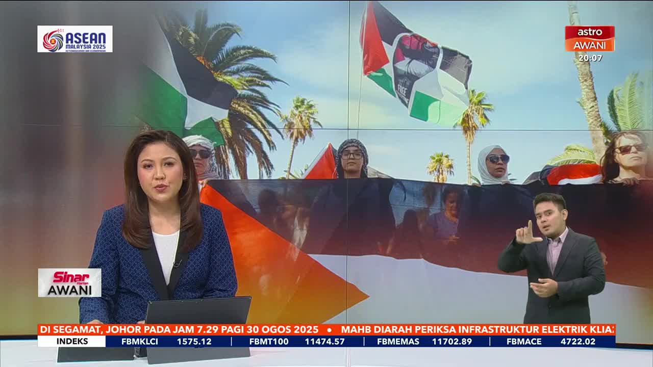 A news anchor in Malaysia, from Astro Awani, speaks to the camera. Behind her, a screen displays a protest with people holding Palestinian flags.
