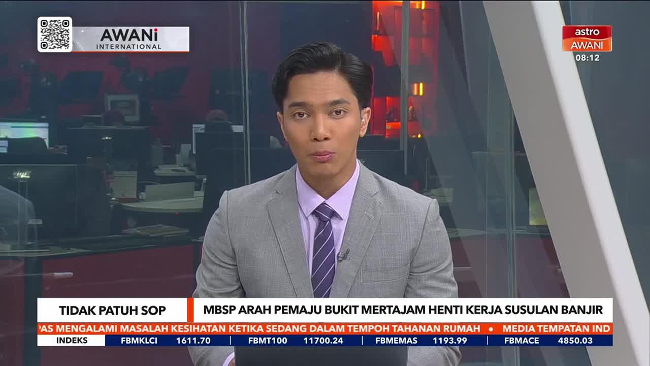 The Astro Awani news anchor, wearing a gray suit and purple tie, is looking directly at the camera. The lower third of the screen displays news headlines in Malay.

