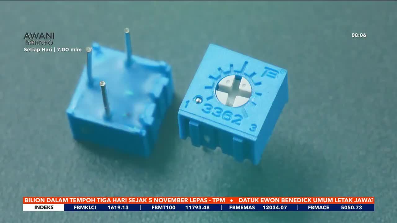Two small, blue electronic components sit side-by-side, each with three silver pins protruding. The Astro Awani Borneo broadcast is running, with financial data scrolling at the bottom of the screen.
