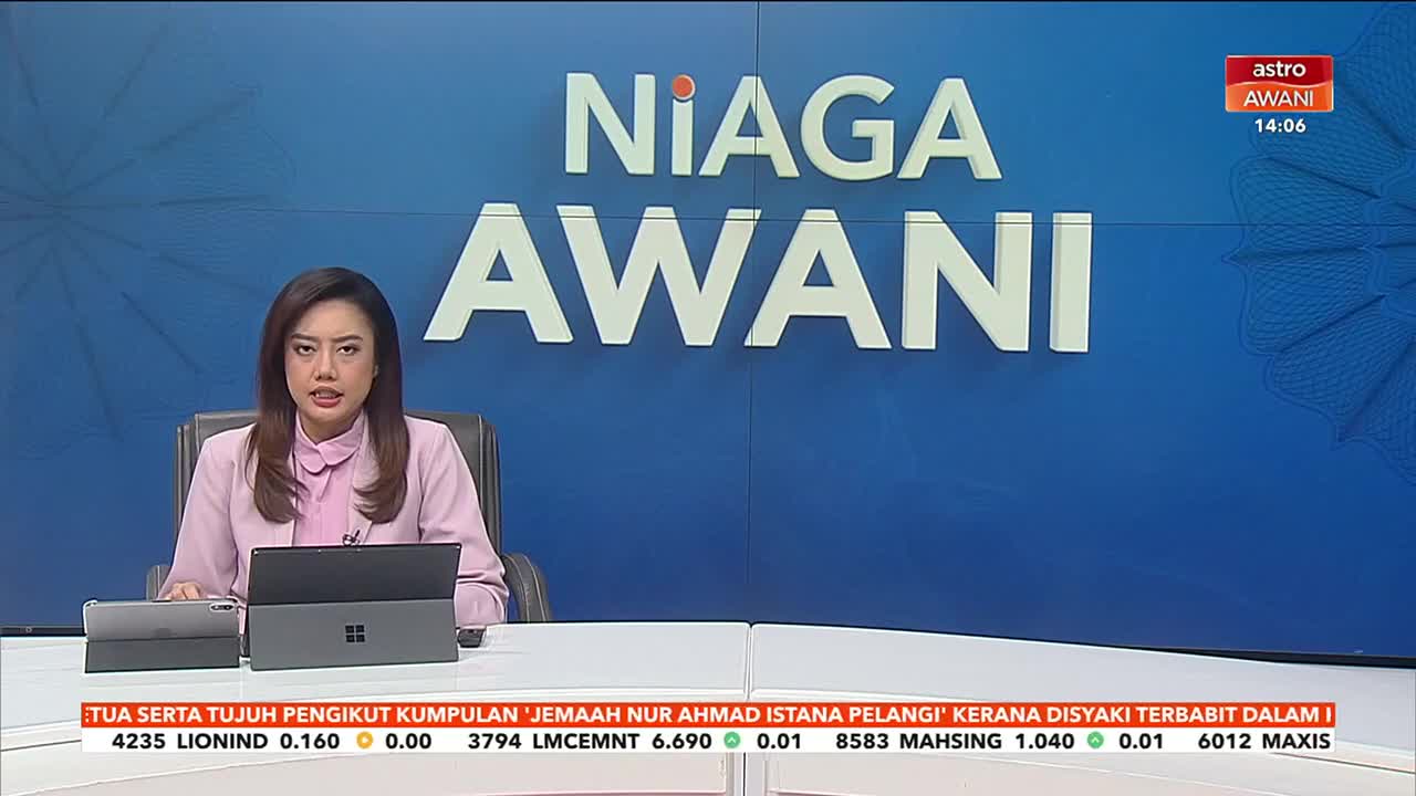 A woman in a pink blazer sits behind a desk, speaking directly to the camera on Astro Awani. Behind her, the words "Niaga Awani" are displayed in large white letters against a blue backdrop.
