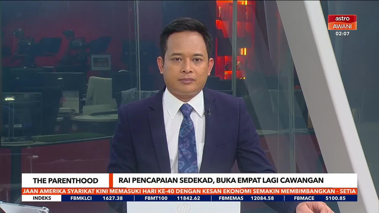 A man in a navy suit and patterned tie is looking directly at the camera. The Astro Awani logo is visible in the corner, and a ticker with financial data scrolls beneath him.
