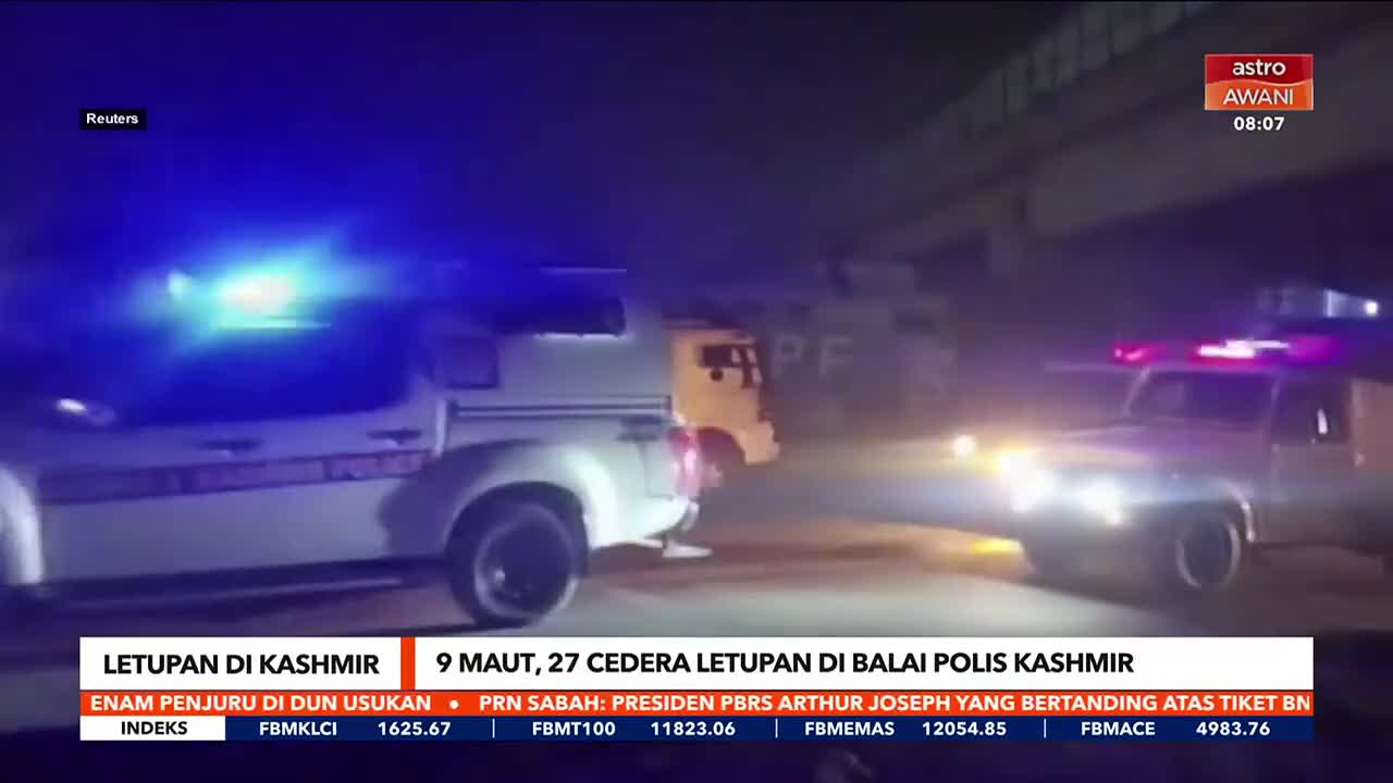 Two police vehicles, their blue and red lights flashing, are parked on the street. The Astro Awani logo is visible in the corner, and a news ticker at the bottom reads about an explosion in Kashmir.
