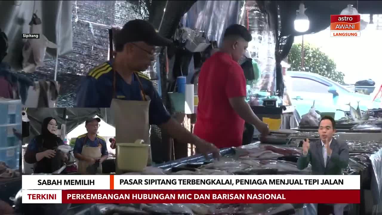 At a market in Sipitang, Sabah, two men are working behind a counter of fish, while a news anchor from Astro Awani reports live. The broadcast is covering the state of the market and the vendors selling roadside.
