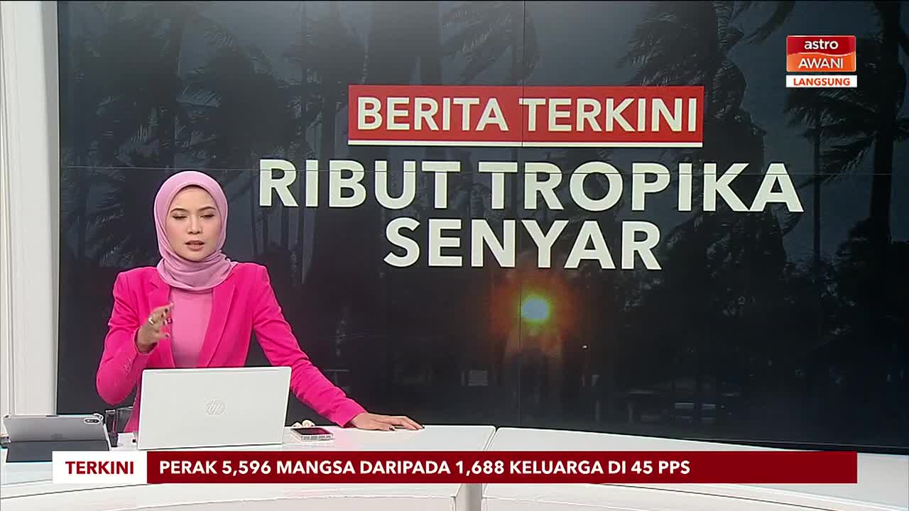 A woman in a pink hijab and blazer gestures with her hand as she speaks. Behind her, the Astro Awani screen displays the headline "Tropical Storm Silent" in Malay.
