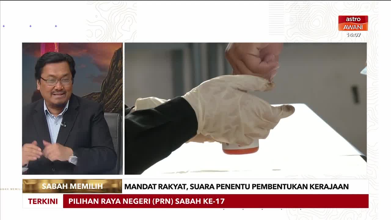 On the Astro Awani broadcast from Malaysia, a gloved hand presses a stamp onto a ballot. The Sabah election is being covered, with a presenter in the corner discussing the process.
