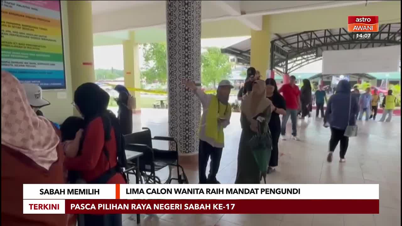 People are lined up, waiting, some holding children, with a man in a yellow vest directing them. The Astro Awani logo in the corner indicates this is likely coverage of the Sabah elections.
