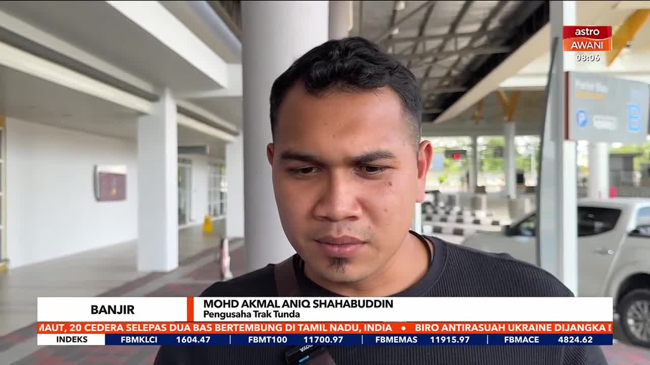 A man is speaking, his expression serious, as the Astro Awani logo and news ticker are visible below. Behind him, a toll booth and a white car are partially in view.
