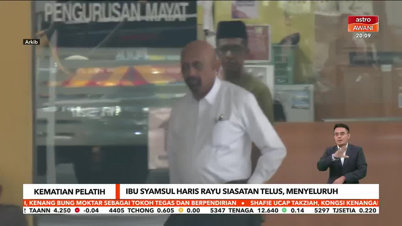 A man in a white shirt walks forward, followed closely by another man. The Astro Awani broadcast shows a news anchor speaking, while the bottom of the screen displays a headline about a death.

