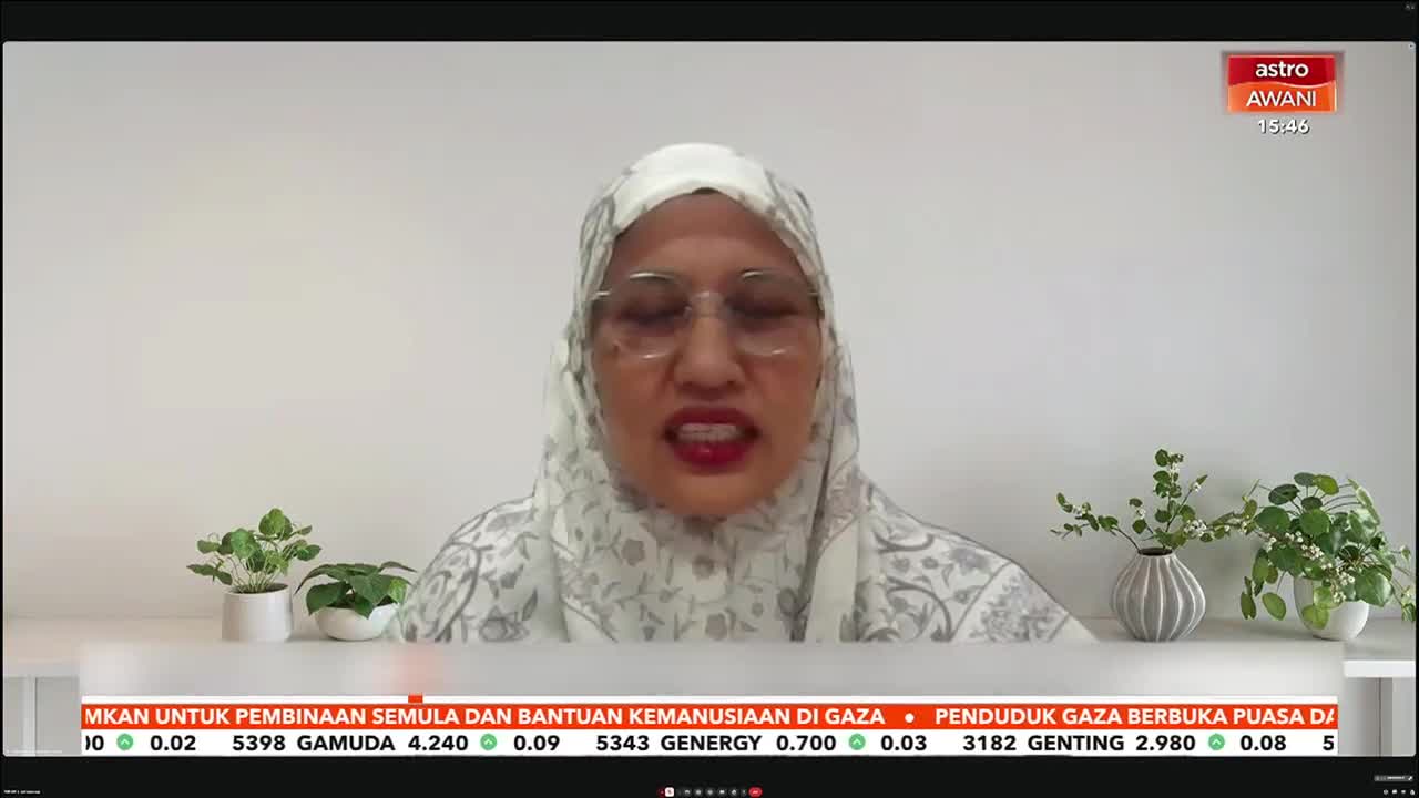 A woman speaks into a camera, her headscarf patterned with a delicate grey design. Below her, a ticker displays stock information and news headlines from Astro Awani. A woman speaks into a camera, her headscarf patterned with a delicate grey design. Below her, a ticker displays stock information and news headlines from Astro Awani.