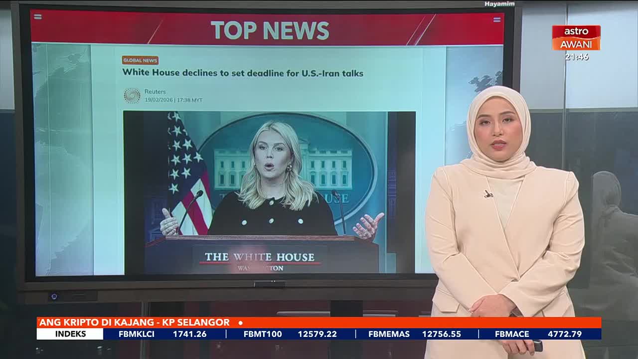 A woman in a cream hijab and suit stands before a large screen displaying "TOP NEWS" and a report about the White House. The screen shows a woman speaking at a podium with the American flag and the White House behind her. A woman in a cream hijab and suit stands before a large screen displaying "TOP NEWS" and a report about the White House. The screen shows a woman speaking at a podium with the American flag and the White House behind her.