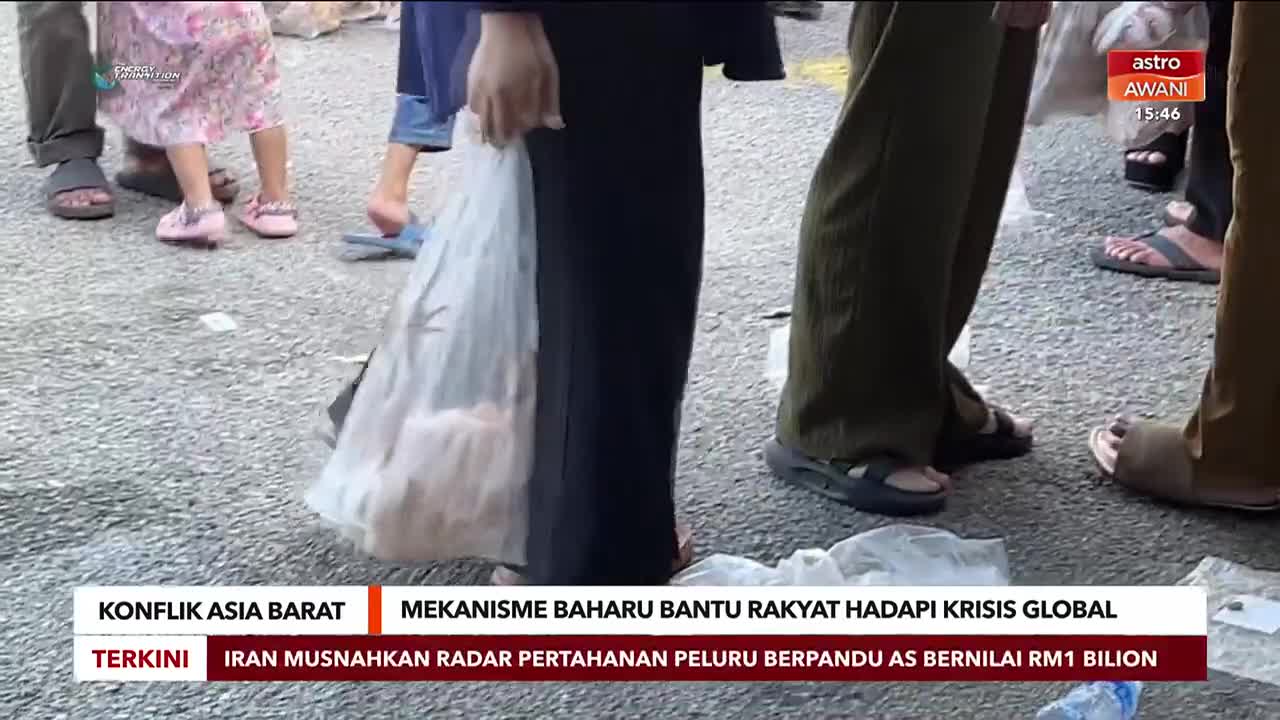 People are gathered, some carrying plastic bags filled with what looks like groceries. A screen in the background displays "astro AWANI" with a timestamp.