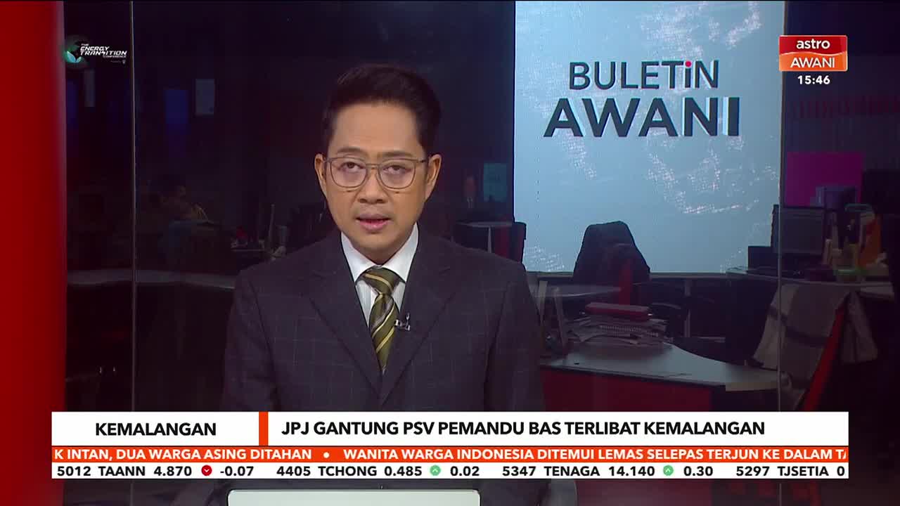 A man in a suit and tie stands before a screen displaying "BULETIN AWANI." Below him, a ticker scrolls with news headlines in Malay.