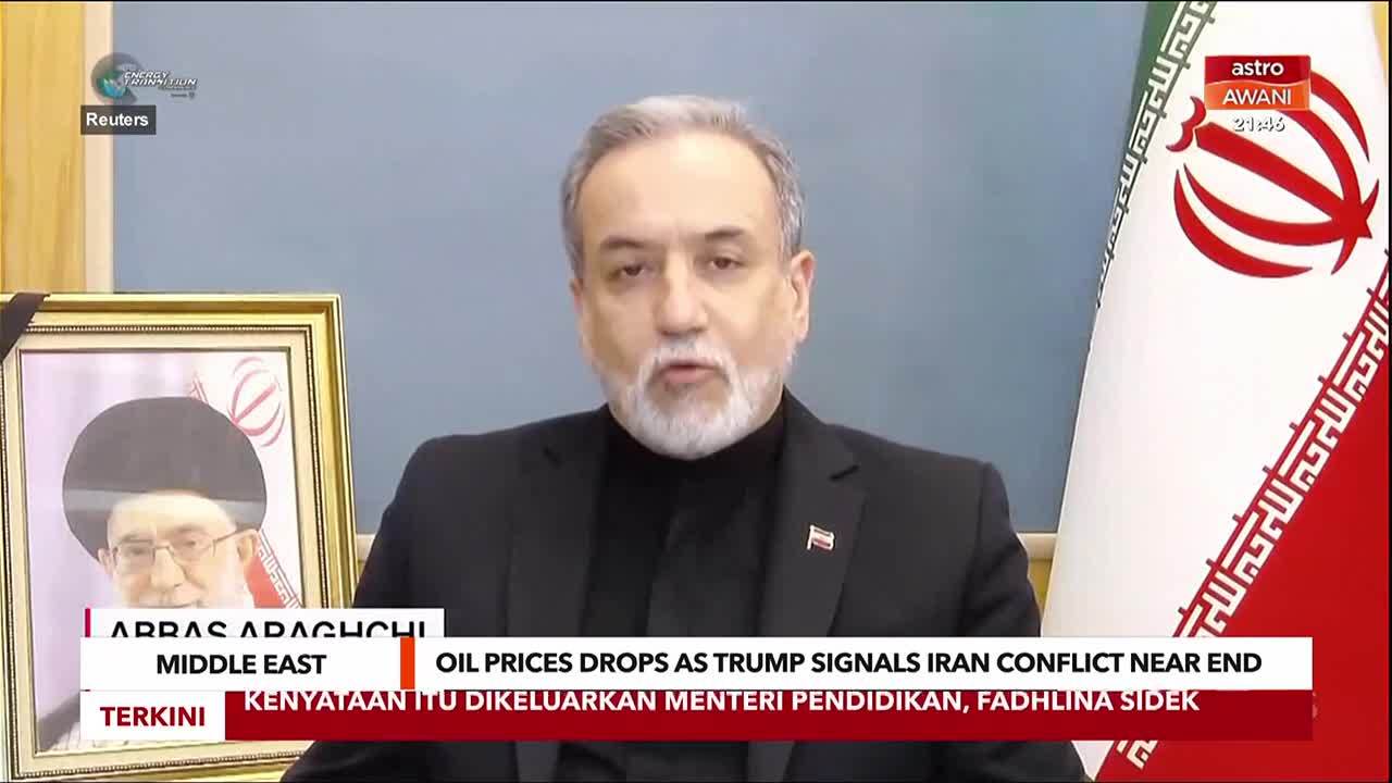 A man with a beard speaks directly to the camera, an Iranian flag behind him. A framed portrait of a religious leader sits to his left.