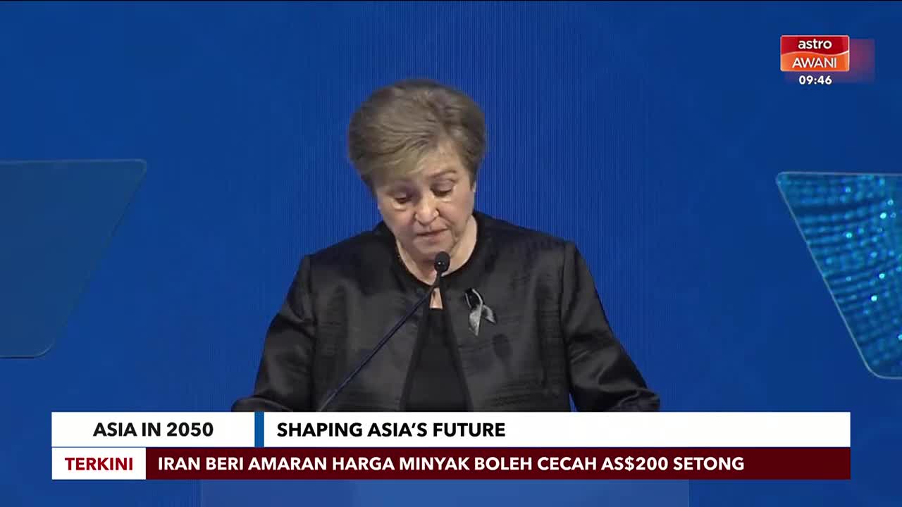 A woman in a black jacket speaks into a microphone, her gaze directed downwards. A ticker at the bottom of the screen displays news from Astro Awani, including a report about Iran's oil price warning.