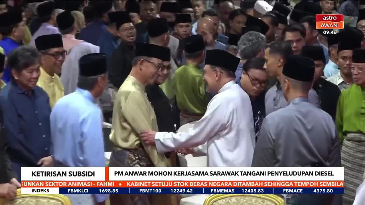 Two men in traditional Malay attire shake hands, a crowd gathered around them. The Astro Awani chyron at the top right indicates this is a formal event in Malaysia.