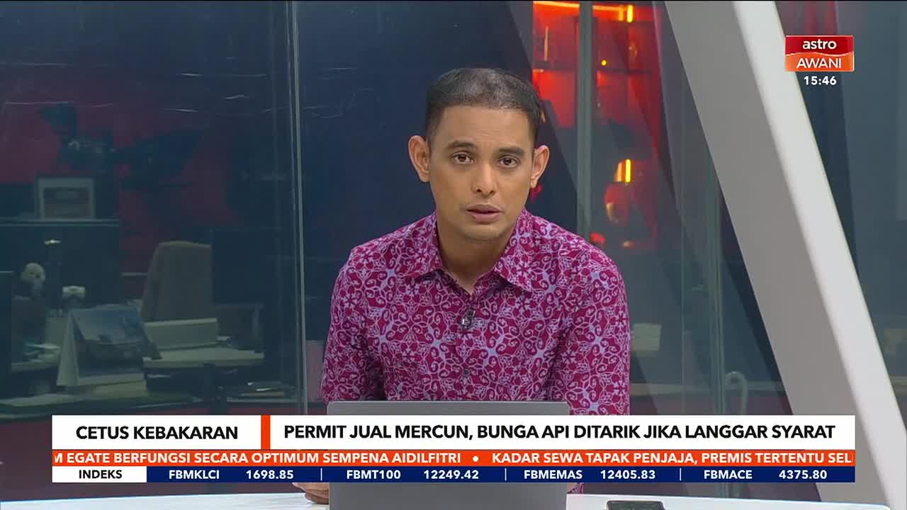 A man in a patterned shirt speaks directly to the camera, his expression serious. Behind him, the Astro Awani logo is visible on a screen, with a ticker displaying financial data.