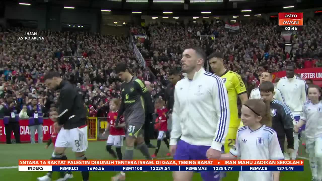 Players in white and yellow kits walk onto the field, escorted by children in red and white. The crowd in the stands is a sea of faces, cheering them on.