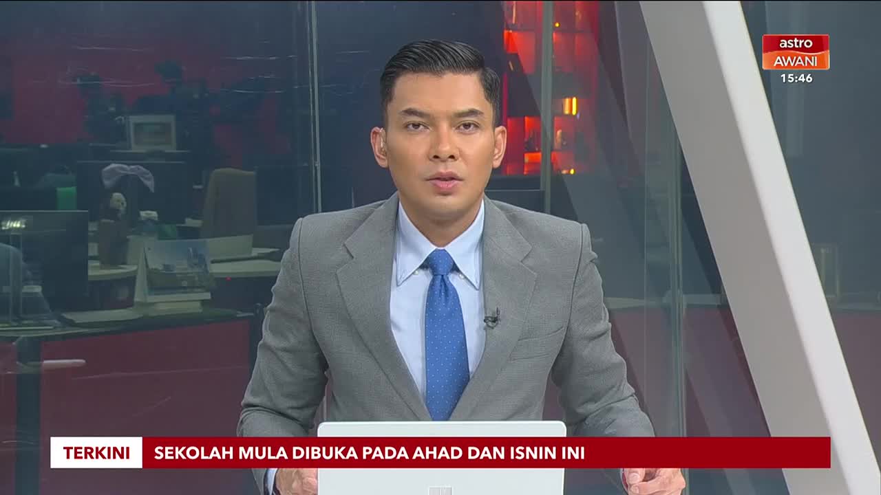 A news anchor in a grey suit and blue tie speaks directly to the camera, with the Astro Awani logo visible in the upper right corner. A red banner at the bottom of the screen displays text in Malay, indicating the latest news.