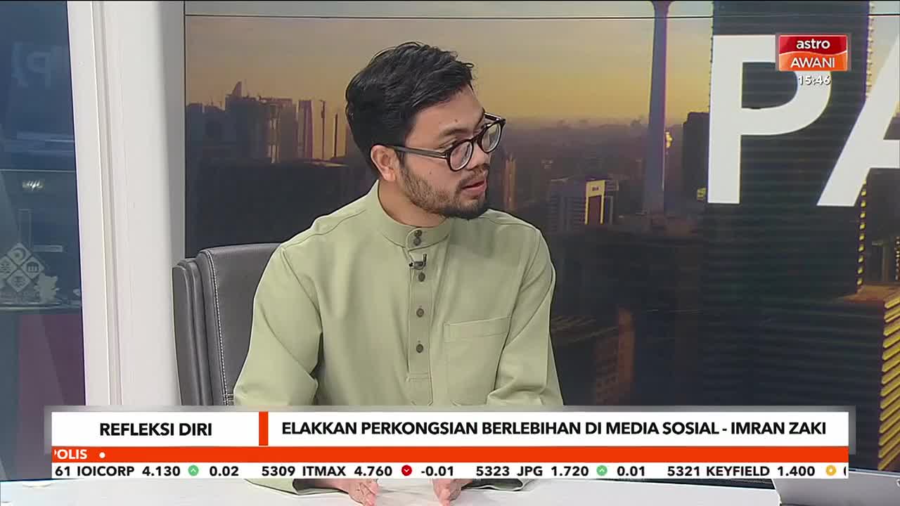 A man in a light green Baju Melayu speaks into a microphone on a television set. The Astro Awani logo is visible in the upper right corner.