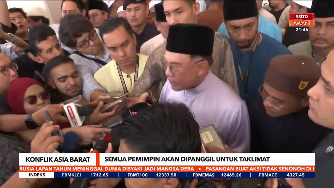 A man in a light purple tunic and black peci is surrounded by reporters, their microphones and phones held out. The Astro Awani chyron at the bottom indicates this is a news event in Malaysia.