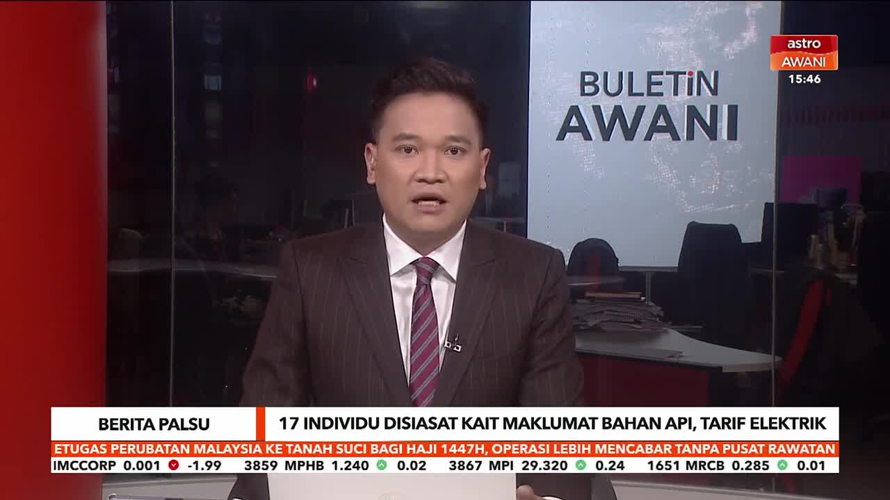 A man in a pinstripe suit stands before a screen displaying "BULETIN AWANI." Below him, a ticker scrolls with news headlines from Malaysia.