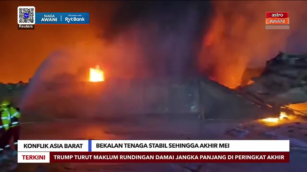 Firefighters spray water onto a large, burning structure as thick smoke billows into the night sky. Flames erupt from the building, casting an orange glow over the scene.