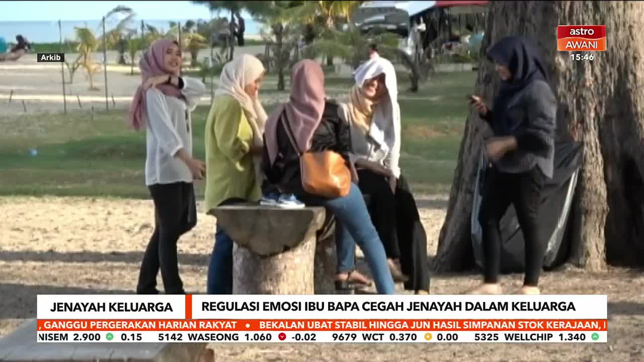 A group of women in hijabs are gathered on a beach, some sitting on a stone bench, others standing. One woman on the right is looking at her phone, while others chat and gesture. The Astro Awani news ticker scrolls across the bottom of the screen.