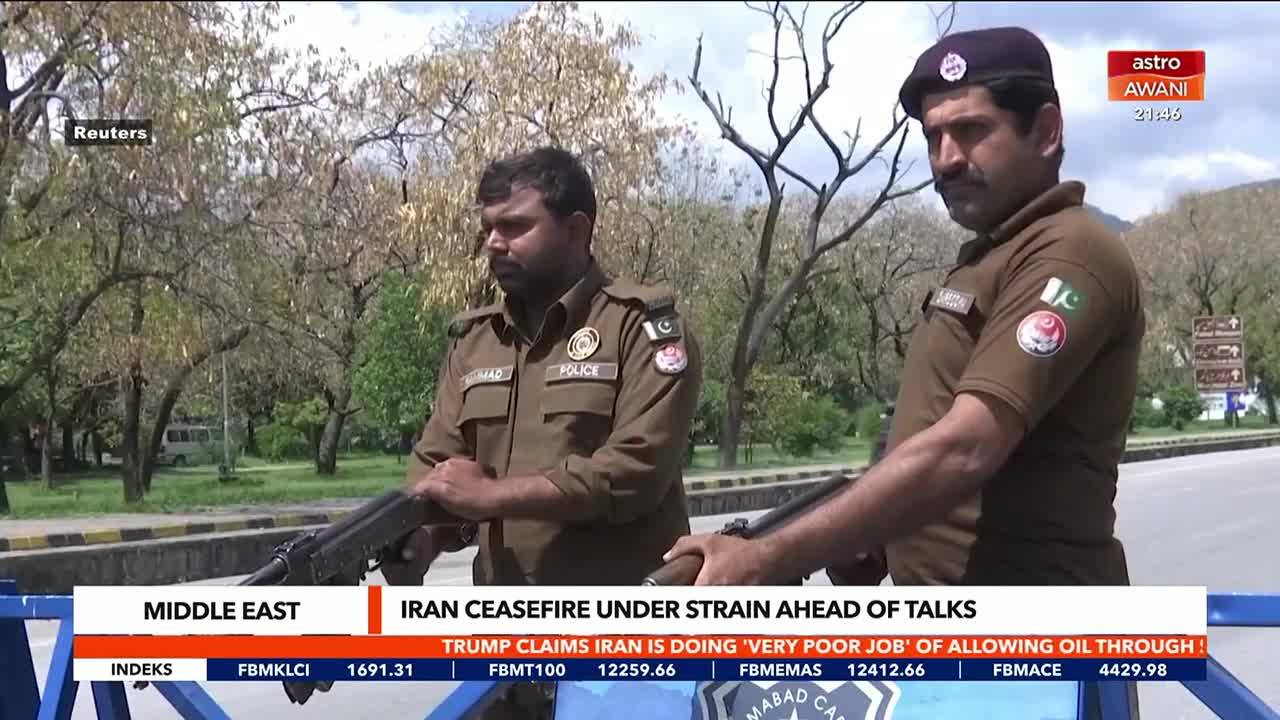 Two police officers stand guard, their rifles held ready. Behind them, a news ticker from Astro Awani reports on a fragile ceasefire in the Middle East.