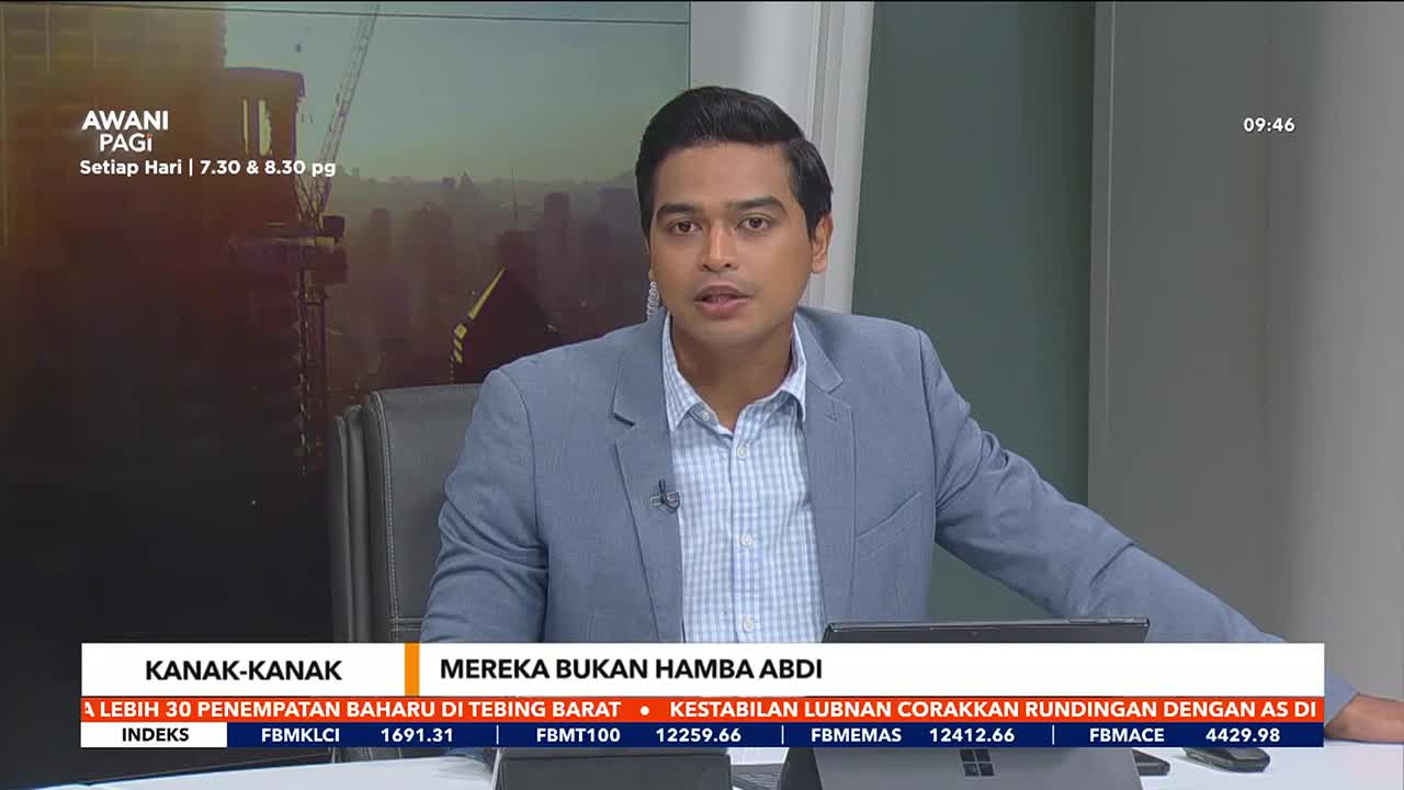 A news anchor in a light blue suit sits at a desk, speaking directly to the camera. Behind him, a screen displays the Astro Awani logo and a cityscape.