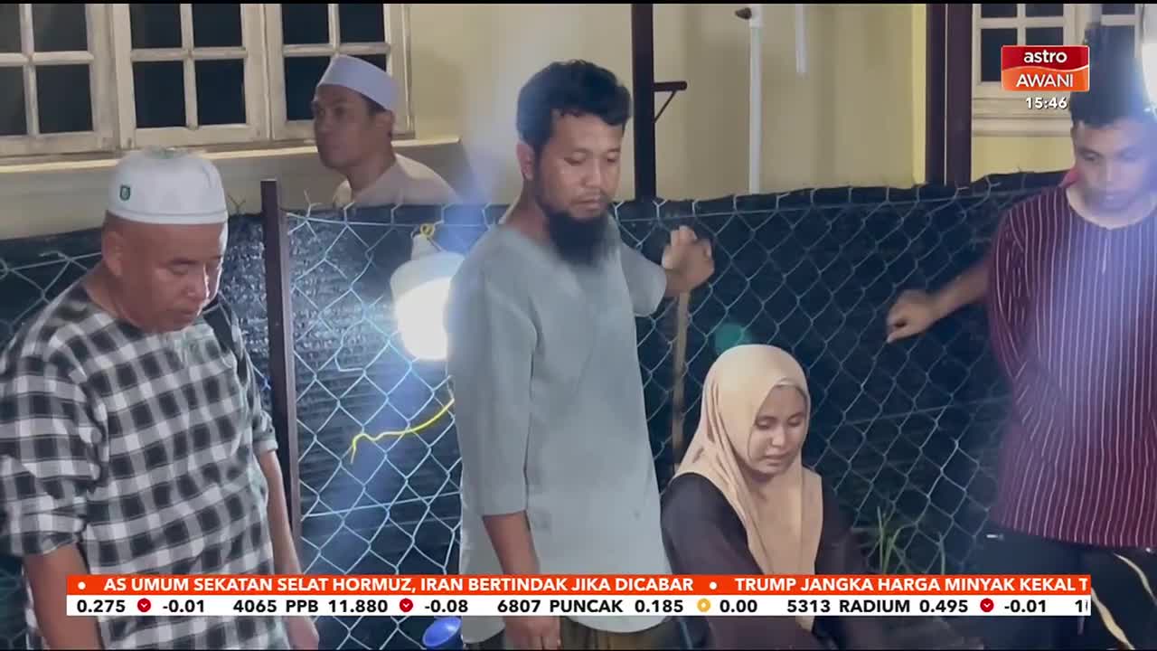 A group of people stand behind a chain-link fence, their faces turned downwards. The Astro Awani logo is visible in the upper right corner.