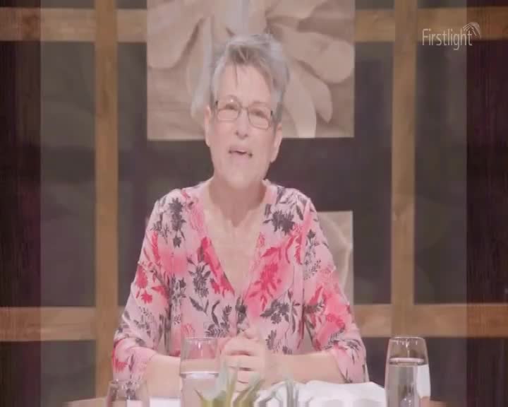 A woman with glasses and a floral top is speaking, her expression animated. The "Firstlight" logo is visible, suggesting this is a broadcast from New Zealand.
