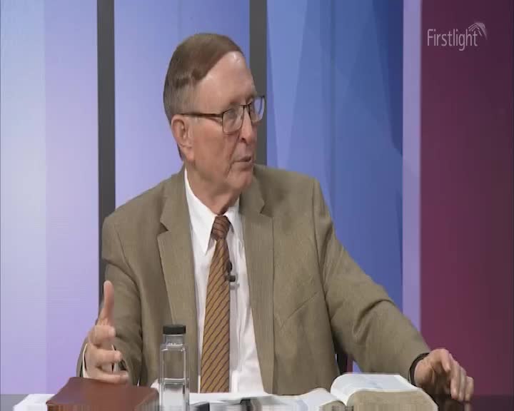 A man in a tan suit gestures with his left hand as he speaks. The Firstlight logo is visible in the background, above a color-blocked backdrop.
