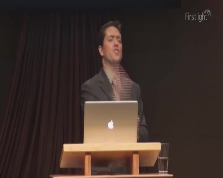 A man in a suit gestures emphatically from behind a podium, his face animated. A Firstlight logo is visible in the corner.
