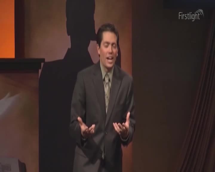 A man in a suit gestures with open hands, speaking with visible emotion. Behind him, a large silhouette looms on a dark backdrop, and the Firstlight logo is visible in the corner.
