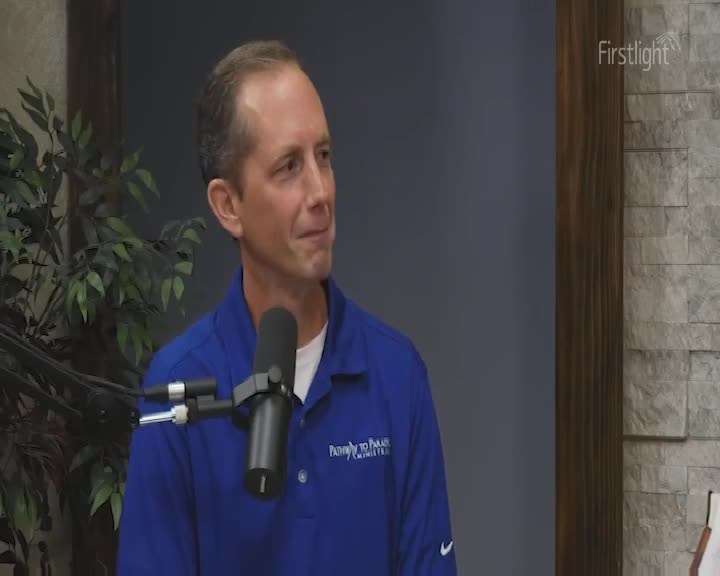 A man in a blue shirt with a microphone in front of him is looking off to the side. The Firstlight logo is visible in the upper right corner.
