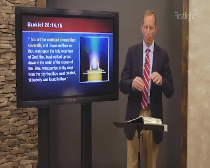 A man in a blazer and tie stands at a lectern, gesturing with his hands as he speaks. Behind him, a screen displays a passage from Ezekiel, accompanied by an illustration.
