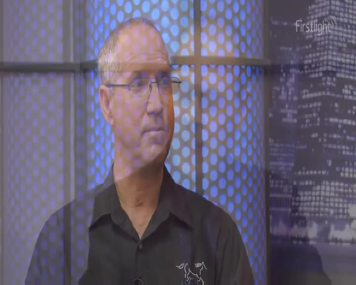 A man in a black shirt, wearing glasses, is looking off to the side. The Firstlight logo is visible in the corner, with a backdrop of blue polka dots and a city skyline.
