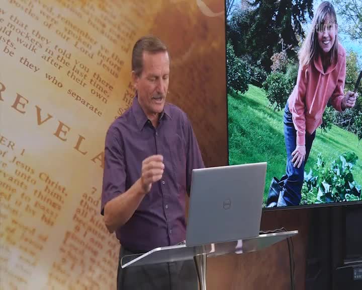 A man in a purple shirt gestures emphatically while speaking at a podium. On the screen behind him, a woman grins while holding a trowel in a garden.
