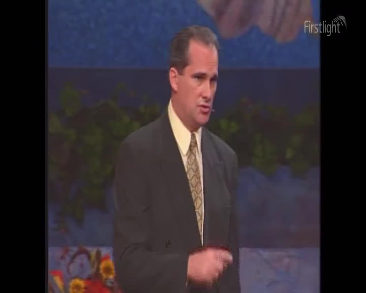 A man in a suit, with a patterned tie, gestures with his right hand as he speaks. The Firstlight logo is visible in the top right corner.
