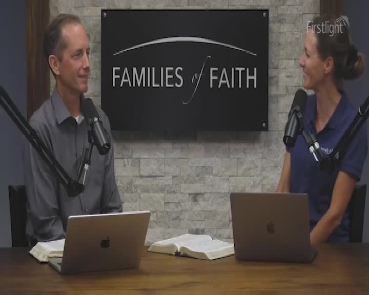 Two people sit at a table, facing each other, each with a microphone in front of them. A laptop and an open book sit on the table between them, as they appear to be in a studio for Families of Faith, a Firstlight production.
