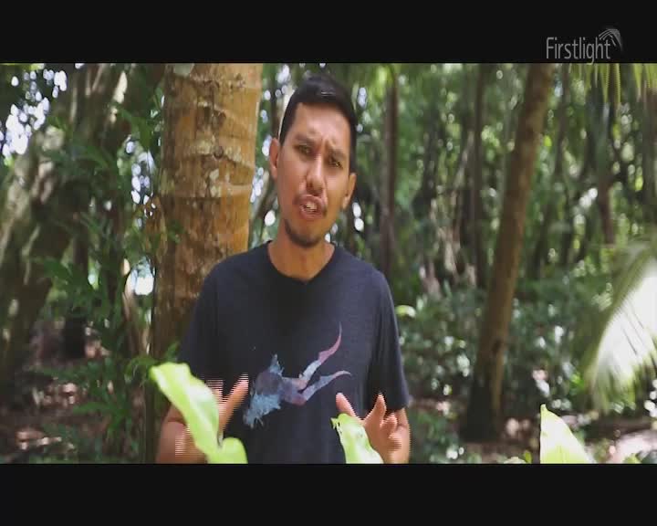 A man in a black t-shirt is speaking, gesturing with his hands in front of a lush, green backdrop. The Firstlight logo sits in the corner as he talks, framed by the natural environment.
