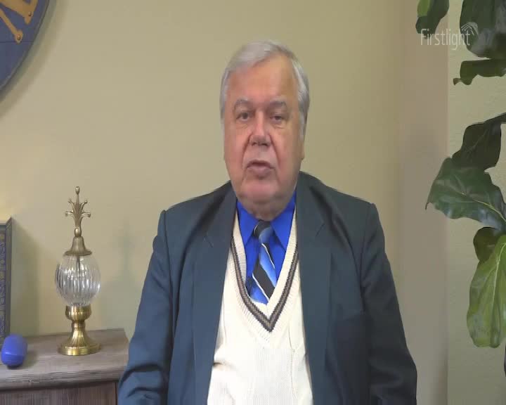 A man in a blue suit jacket and a striped tie is speaking directly to the camera. The "Firstlight" logo is visible in the upper right corner.
