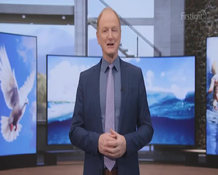 A man in a blue suit stands in front of three large screens, speaking to the camera. The Firstlight logo is visible, and the screens behind him display images of a dove, water, and a person.
