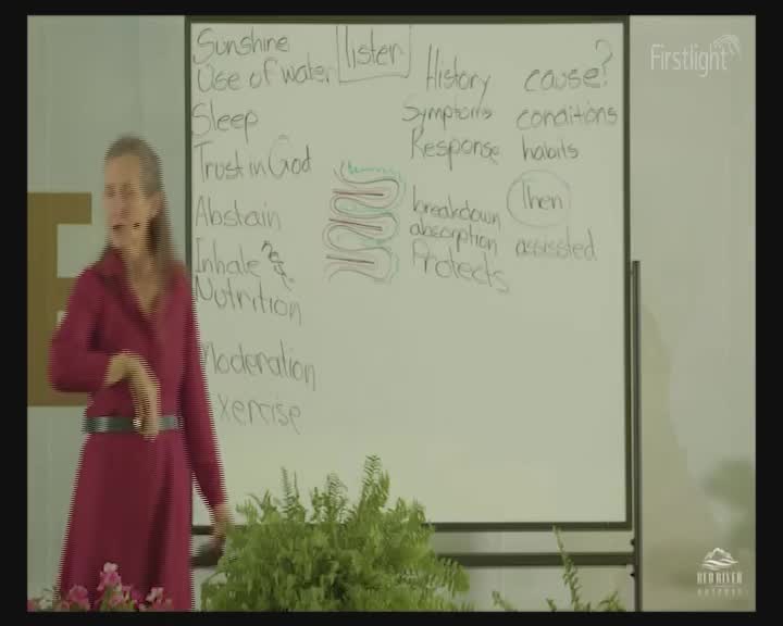 A woman in a red coat gestures towards a whiteboard covered in handwritten notes. The Firstlight logo is visible in the corner of the screen.
